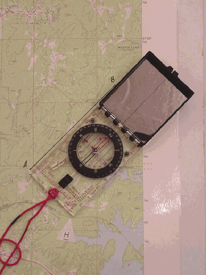 Compass placed on a topographic map with its edge aligned from Point A to Point B.